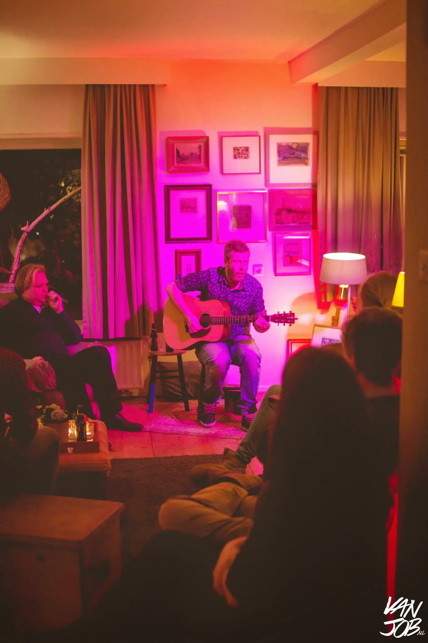 Ed Struijlaart speelt gitaar in een huiskamer — staand portret met publiek op de voorgrond